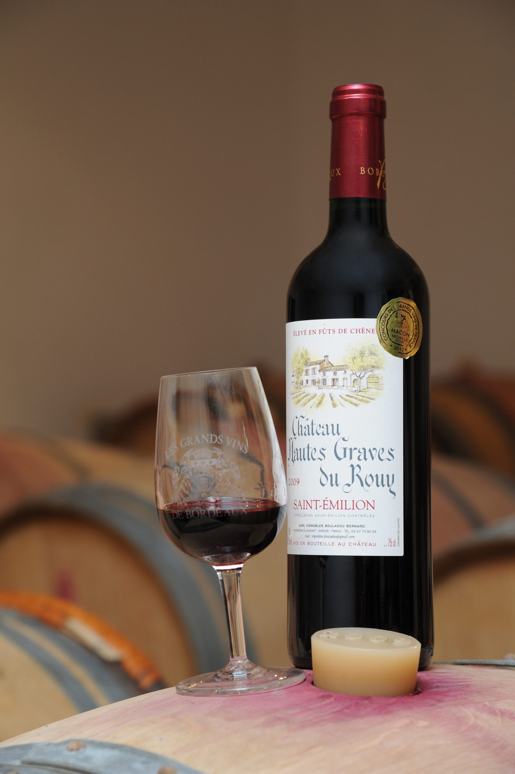 Bouteille du Château Hautes Graves du Rouy avec un verre posés sur une barique